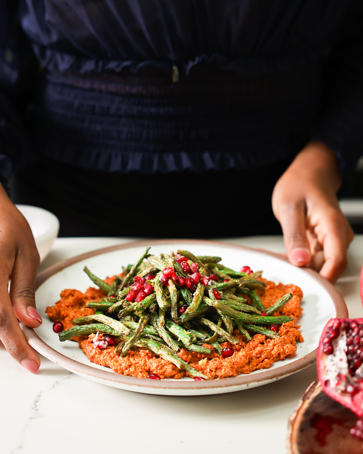 Jenné serving air fryer green beans on a plate of muhammara.