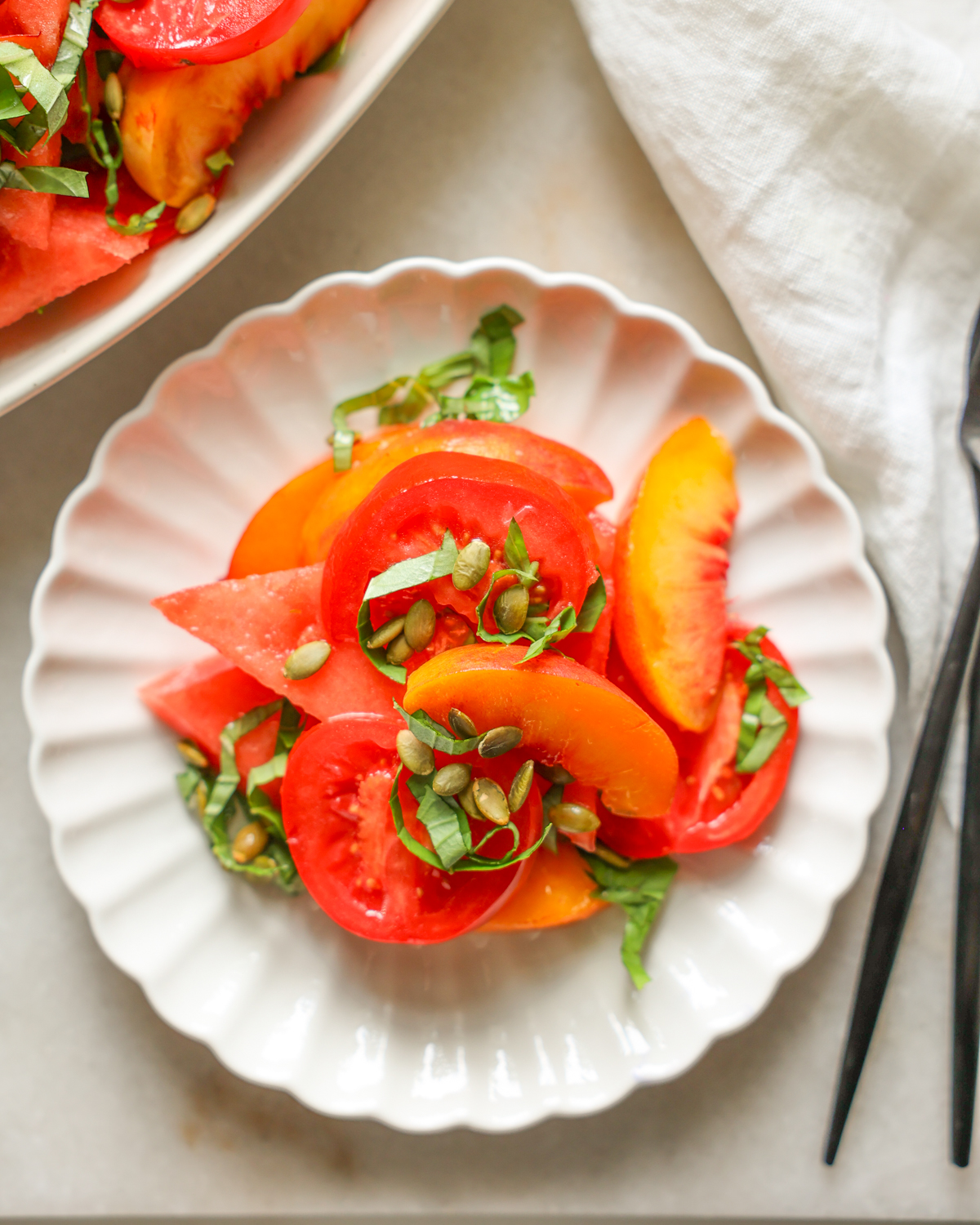 Watermelon salad with peaches and basil on a white plate.