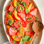 Peach and Watermelon Salad with basil and pumpkin seeds on a large white platter.