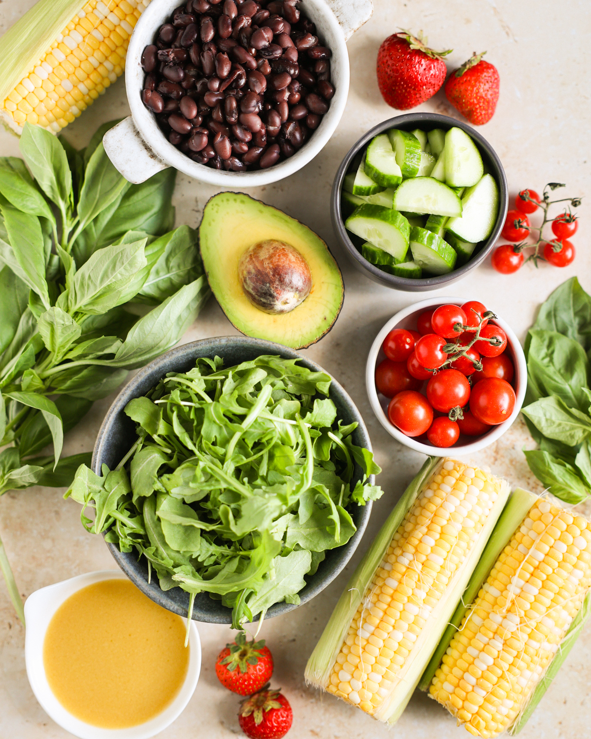 Summer salad ingredients, including corn, avocado, black beans, and basil, on the counter.