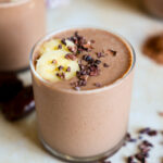 Chocolate smoothie topped with banana in a glass.
