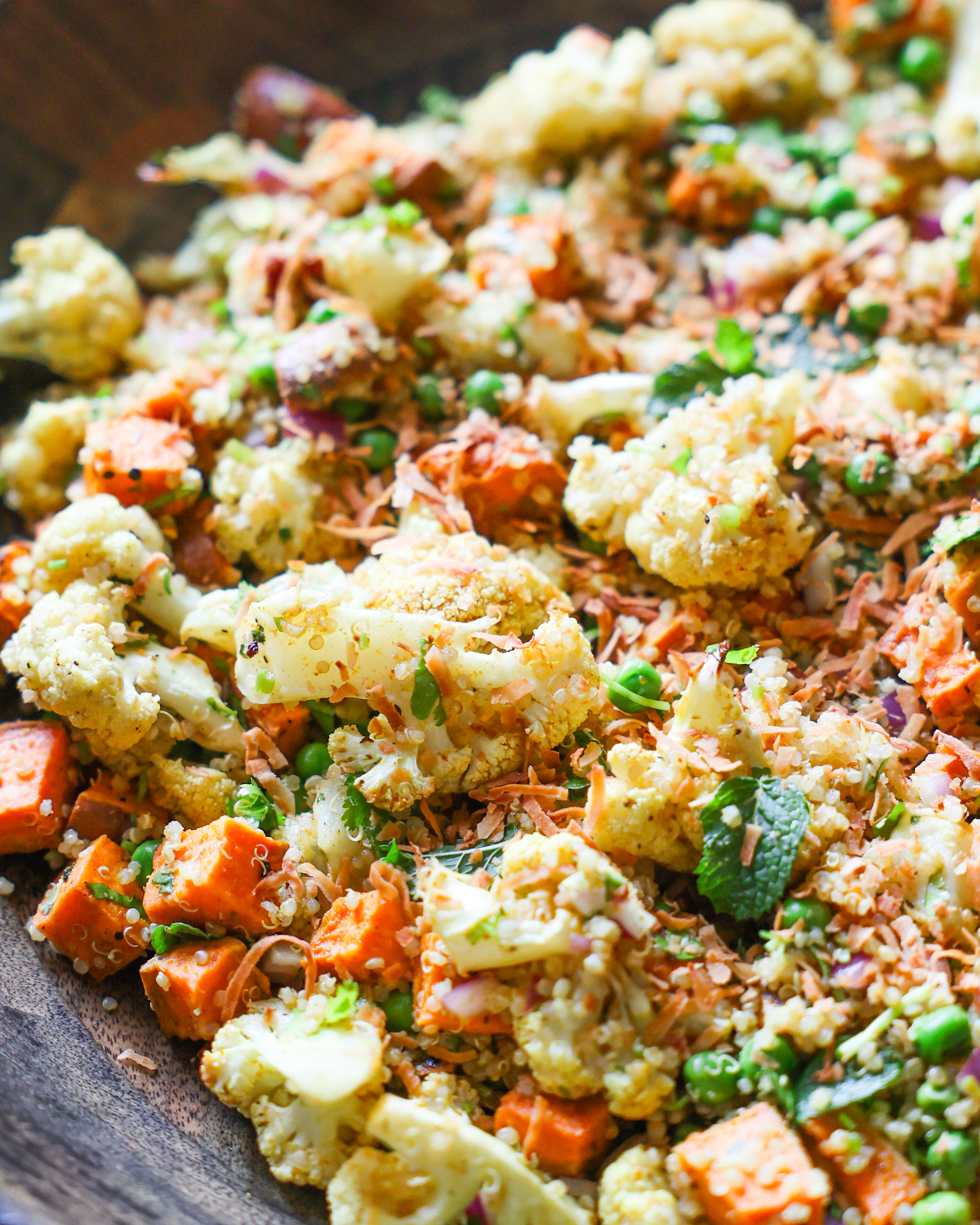 Cauliflower salad in a bowl with visible sweet potatoes, peas, and herbs.